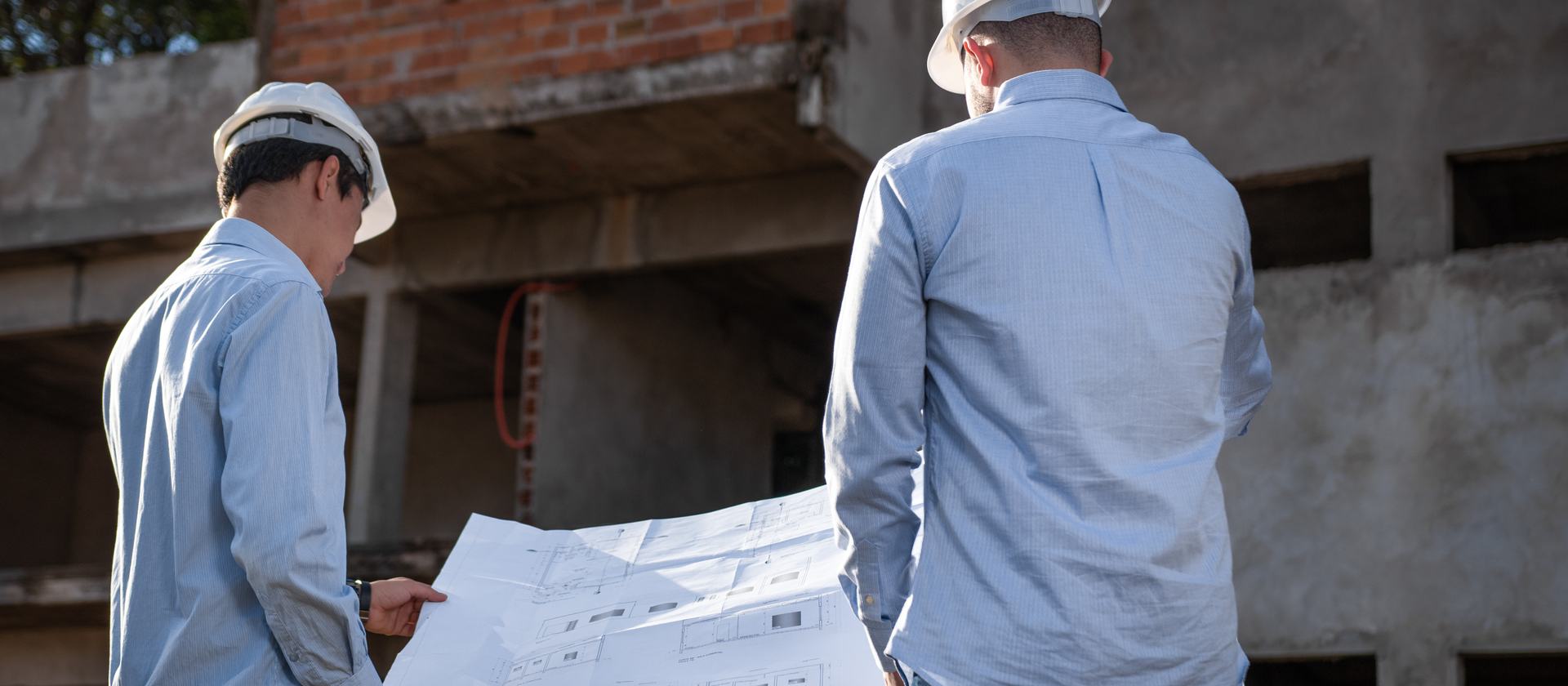Engenheiros conferindo a planta em frente a uma obra
